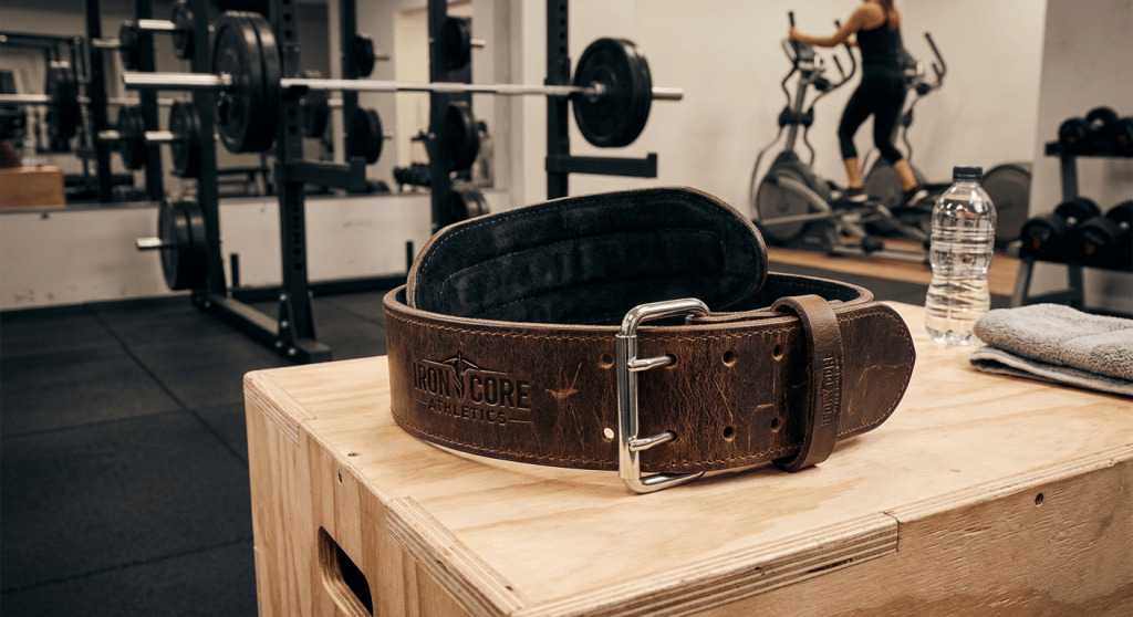 Brown lifting belt labeled “IRON CORE ATHLETICS” on a wooden gym box